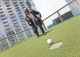 African American Businessman Playing Golf on Skyscraper Rooftop