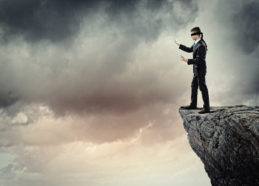 Image of businessman in blindfold standing on edge of mountain